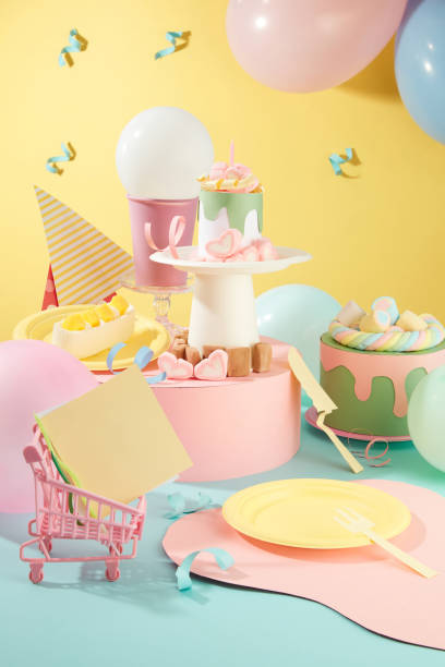 istock Front view of note pads inside a mini cart, birthday cakes made from brightly decorated paper. Ribbons and balloons are glued on a yellow background. Layout of birthday party. 1957046540