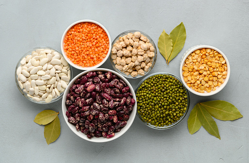 Various sources of vegetable protein: beans, lentils, peas, chickpeas, mung bean in bowls. A healthy balanced diet for vegans and vegetarians. Gray stone background.