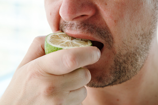 Close up of a man's mouth eating lime, fresh juice full of vitamins. Healthy lifestyle concept, young man eating lemon.