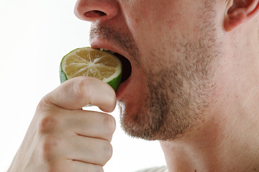 Close up of a man's mouth eating lime, fresh juice full of vitamins. Healthy lifestyle concept, young man eating lemon.