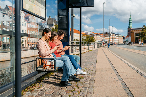 Three young friends using their smart phones while waiting for a bus in Copenhagen in Denmark.