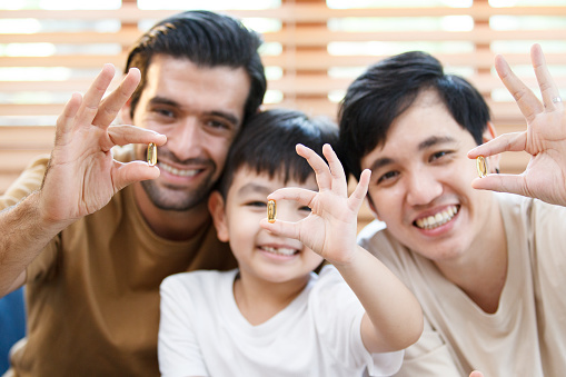 Happy cheerful Asian men and little boy showing the fish oil capsule supplement to camera.