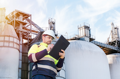 An inspector reviews a large industrial plant, clipboard in hand