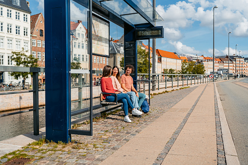 Three young friends waiting for a bus in Copenhagen in Denmark.