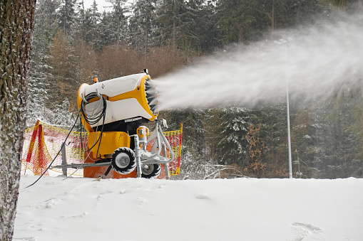Snow cannon makes artificial snow. Snowmaking systems sprays water to produce snow. Preparation of ski track for skiing, winter sport. Machine making snow.