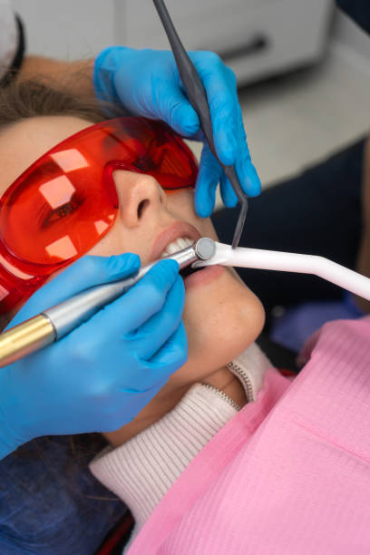 close-up dentist uses a drill and a dental mirror to treat the teeth of a young female patient in protective glasses. concept of dental hygiene and health. vertical photo - dental hygiene dental equipment dental drill practicing photos et images de collection