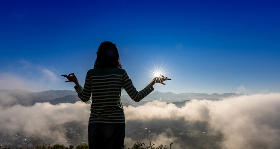 Panorama back view of woman is relaxingly practicing meditation yoga mudra at top of misty mountain with rising sun in summer to attain happiness from inner peace wisdom for healthy mind and soul