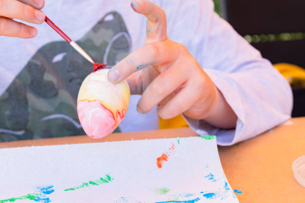 istock 11-year-old boy painting an Easter egg with watercolors in his backyard. 1957146275