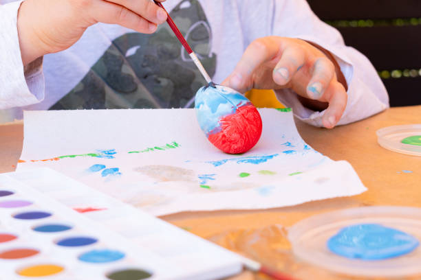 istock 11-year-old boy painting an Easter egg with watercolors in his backyard. 1957146869