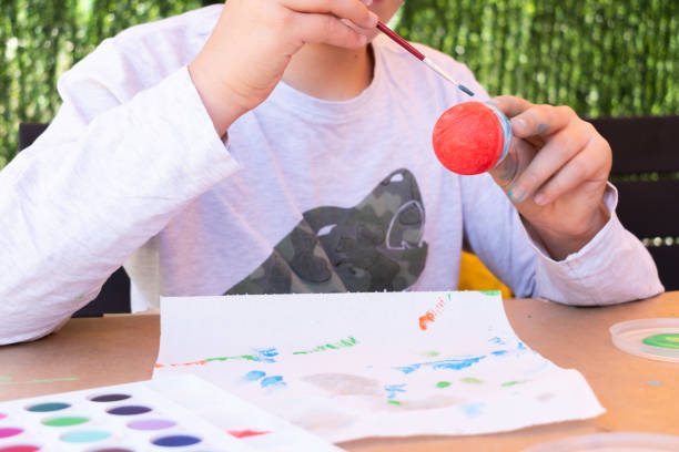 istock 11-year-old boy painting an Easter egg with watercolors in his backyard. 1957147408