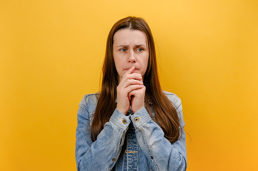 Portrait of exhausted nervous young woman showing mind explosion gesture, feeling unhappy, lots unnecessary information, wearing denim jacket, posing isolated on yellow color background wall in studio