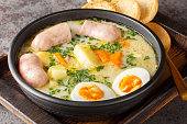 Polish zurek a rich soup soured with fermented rye starter, served with a boiled halved egg and a meaty white sausage close-up in a bowl. Horizontal
