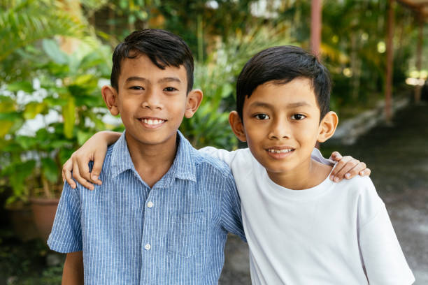 Two boys sit together on a stone bench outdoors, sharing time under the sunlight. Concept of brotherhood, childhood, and peaceful friendship.