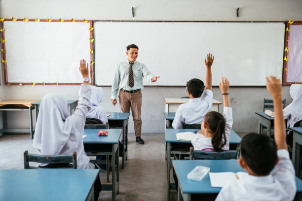 High school students are participating in a lesson, raising their hands to answer a question posed by their teacher