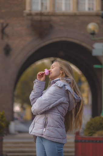 Young blonde woman smelling pink flower on the street