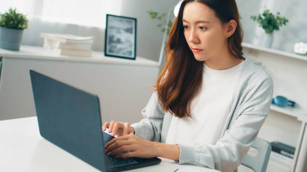 istock Positive young Asian female employee or freelancer using computer laptop, typing on keyboard and working remotely from home, Young employee with multitasking spending time with work at home office 1957208686