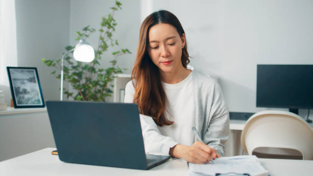 istock Positive young Asian female employee or freelancer using computer laptop, typing on keyboard and working remotely from home, Young employee with multitasking spending time with work at home office 1957209234