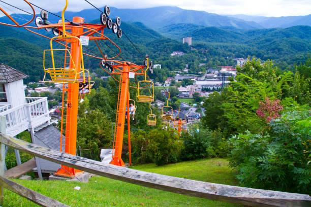 Orange Chairlift over Green Hillside with a View of Mountain Town, Tennessee Experience the breathtaking beauty of Gatlinburg, Tennessee with this vibrant image of a chairlift descending a lush green hillside, offering stunning views of the picturesque mountain town below. Perfect for promoting outdoor recreation and tourism. gatlinburg stock pictures, royalty-free photos & images