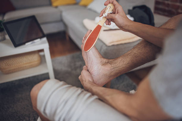 man having foot bath at home and removing dead skin from feet - water lime foto e immagini stock