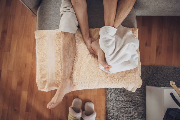 Man relaxing at home and applying lotion on feet after foot bath