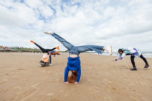 Front view full length of a small group of female teenage friends wearing casual clothing on an overcast summer day in Whitley Bay, Northeastern England. They are practicing cartwheels on the beach.