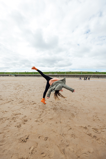 Rear view full length of a female teenager wearing casual clothing on an overcast summer day in Whitley Bay, Northeastern England. She is practicing cartwheels on the beach.