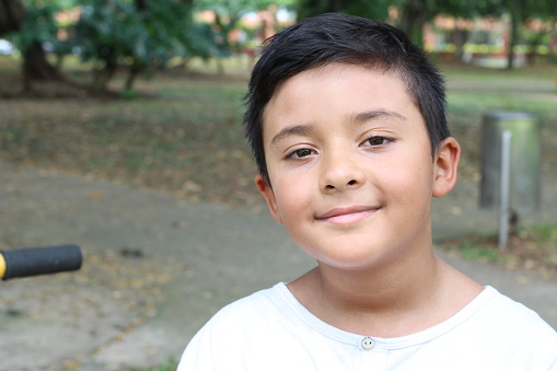 An eight years old cute Colombian boy is smiling at camera. He stands in a public park where he enjoys to play.