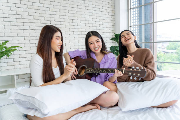 istock Friends are jamming together on a bed, singing and playing guitar. 1957253687