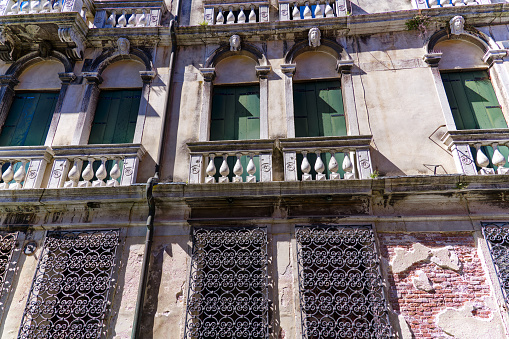 Weathered facade of historic house with wrought iron grids in front of windows at Italian City of Venice on a sunny summer day. Photo taken August 7th, 2023, Venice, Italy.