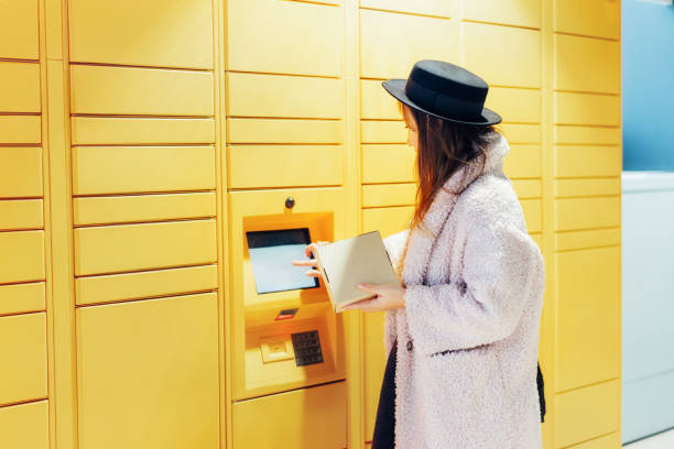 istock Fashion woman with box using modern postal automatic mail terminal with self service device for pickup or refund an order. Electronic locker for storing parcels. Online shopping. Selective focus. 1957269901