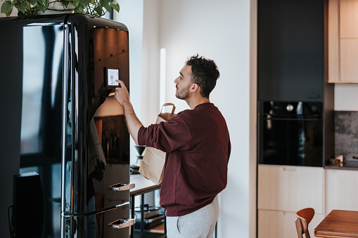 Latin man embraces the future of shopping as he interacts with his smart fridge, seamlessly integrating technology into his daily routine