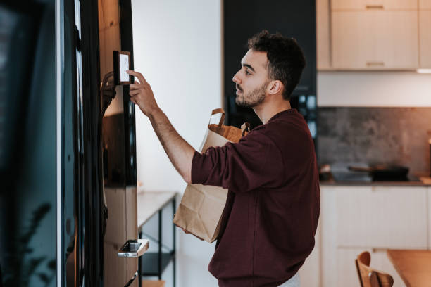 istock Man interacts with his smart fridge, holding a bag filled with fresh groceries 1957273217