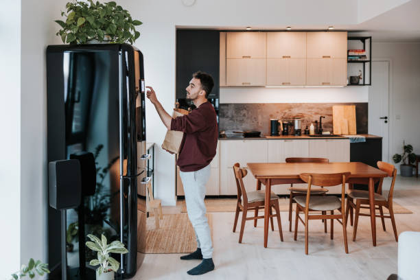 istock Man interacts with his smart fridge, holding a bag filled with fresh groceries 1957273219