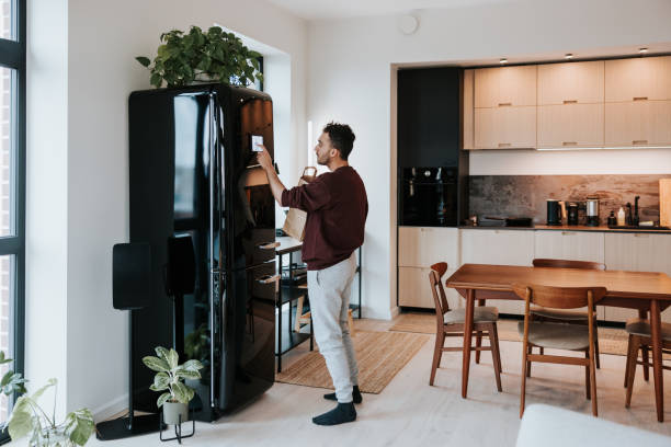 istock Man interacts with his smart fridge, holding a bag filled with fresh groceries 1957273220