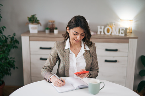 Businesswoman in a modern home office making notes in a notebook