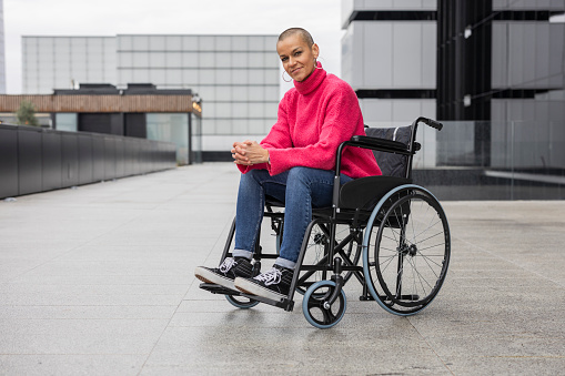 modern bald woman athlete posing looking at camera in her wheelchair smiling and optimistic - empowerment and survivor