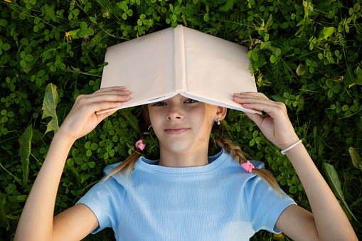 One teen girl student sleeping with book on green grass lawn in park, studies, writes, reads.
