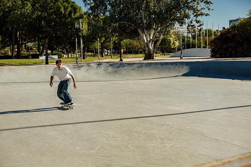 Full body of young male skater in casual outfit doing trick on skateboard riding in skate park