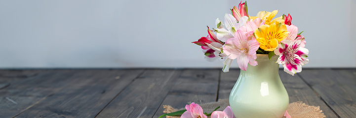 banner of multi-colored blooming alstroemeria flowers in clay vase on wooden table with round napkin and a pink ribbon. the concept of summer, spring, nature bloom, holiday and congratulations. copy space.