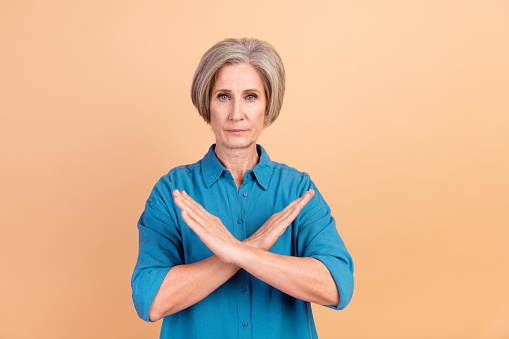 Portrait of strict serious senior person with white gray hairdo holding arms crossed show stop isolated on pastel color background.