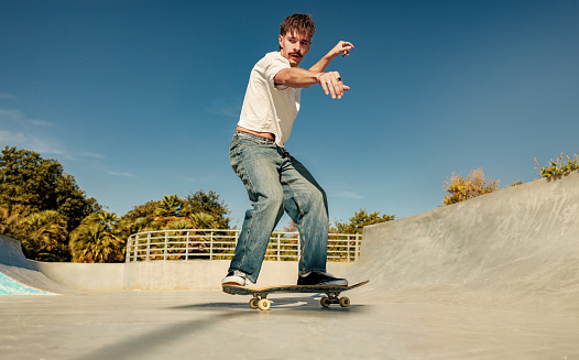 Excited young man riding skateboard in skate park on sunny day. Extreme sport concept