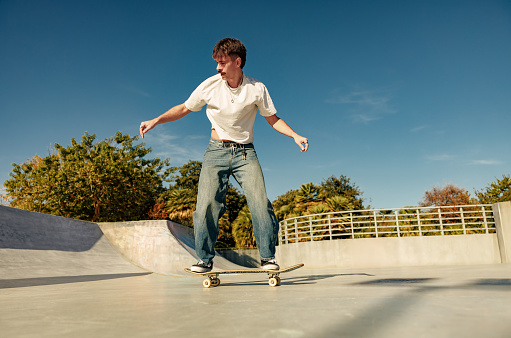 Full body of young male skater in casual outfit doing trick on skateboard riding in skate park