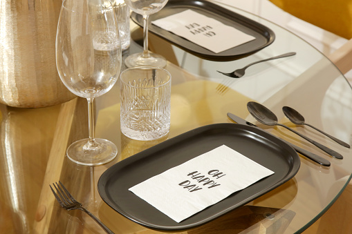 Dining table arrangement with ceramic black rectangular dinner plates, silver flatware set and glasses for water and wine.