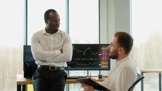 Two diverse traders making professional analysis while sitting in the office in front of multiple computer screens