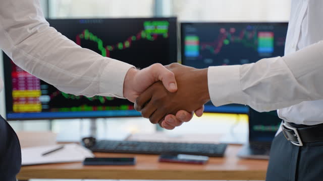Close up of two diverse traders handshake with candlestick forex or cryptocurrency chart on blurry office interior background