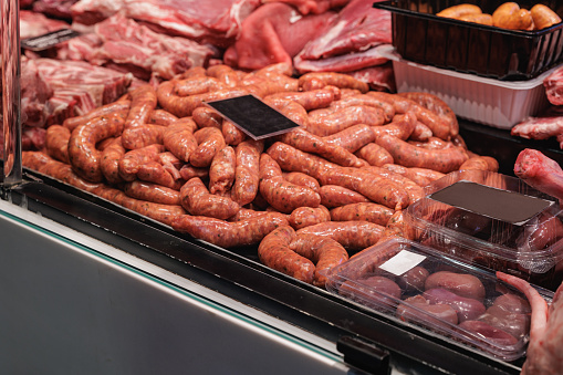 Sausages and fresh meat in glass cabinet displayed for sale on food market stall in Barcelona