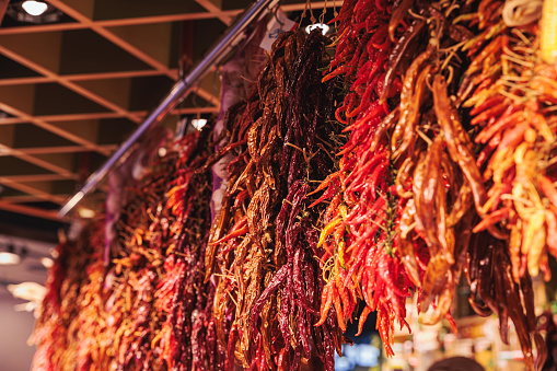 Rows of dried red pepper in bunches tied on strings and hung on food market stall in Barcelona