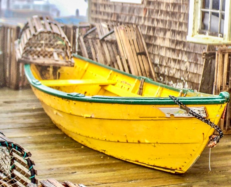 A yellow dory surrounded by old lobster traps in the morning fog.