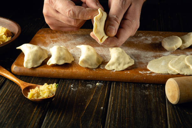 istock The chef is making dumplings with his hands. Step-by-step process of preparing homemade dumplings filled with mashed potatoes on a dark table. Ukrainian cuisine. Close-up view. 1957373774
