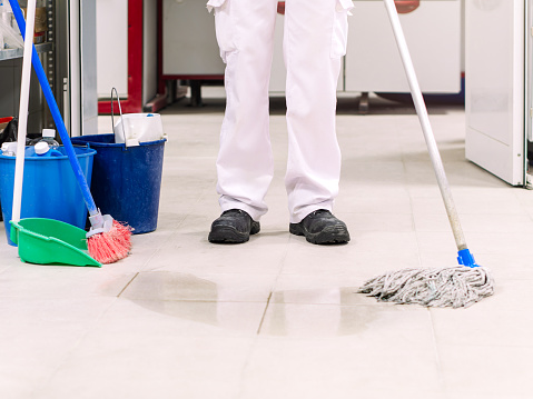 A shot of a mature school janitor, with protective gloves, mopping the floor of the empty school classroom and disinfecting and preventing coronavirus.